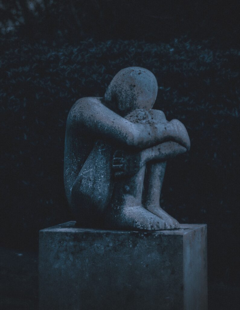 A stone statue of a person sitting with knees bent into their chest